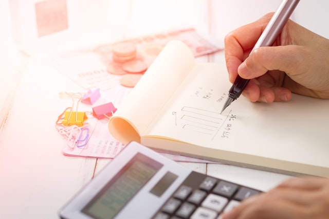 Person taking notes in a notepad and using a calculator to determine the value of multiple rental properties